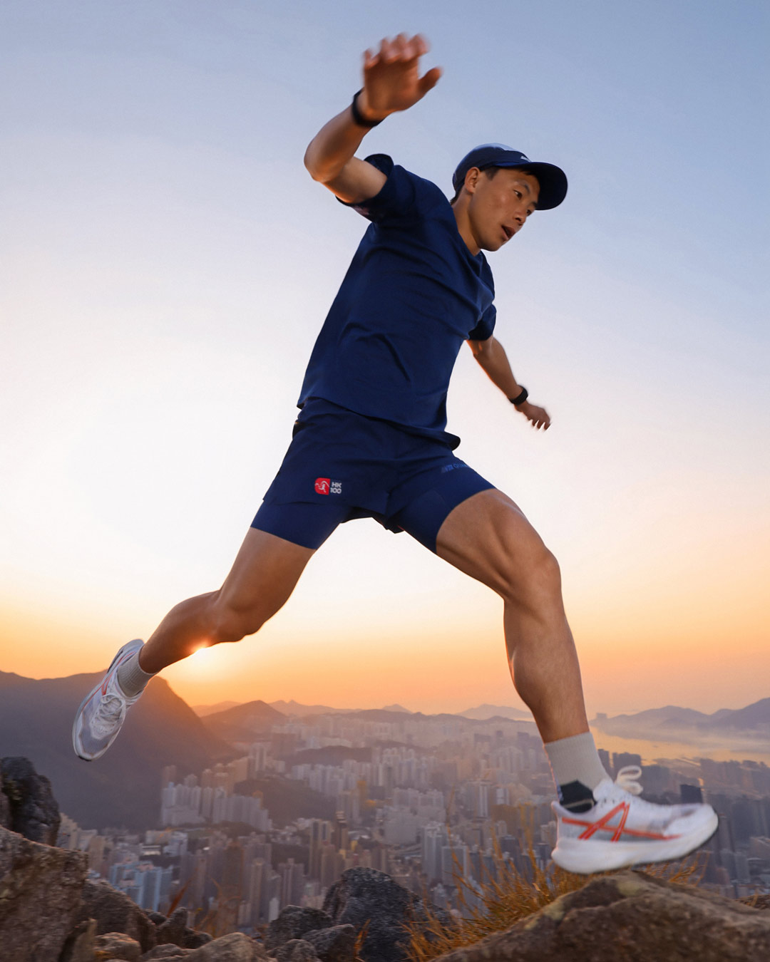 Elite trail runner wearing ANTA GUANJUN 100% Merino wool T-shirt and shorts, jumping across rocky terrain above Hong Kong at sunrise